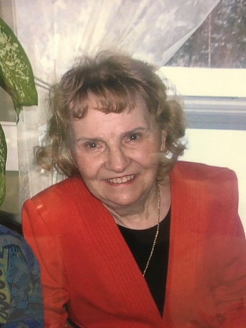 Portrait de Thérèse Rancourt, femme souriante aux cheveux bouclés portant un blazer rouge, photographiée à l'intérieur près d'une fenêtre